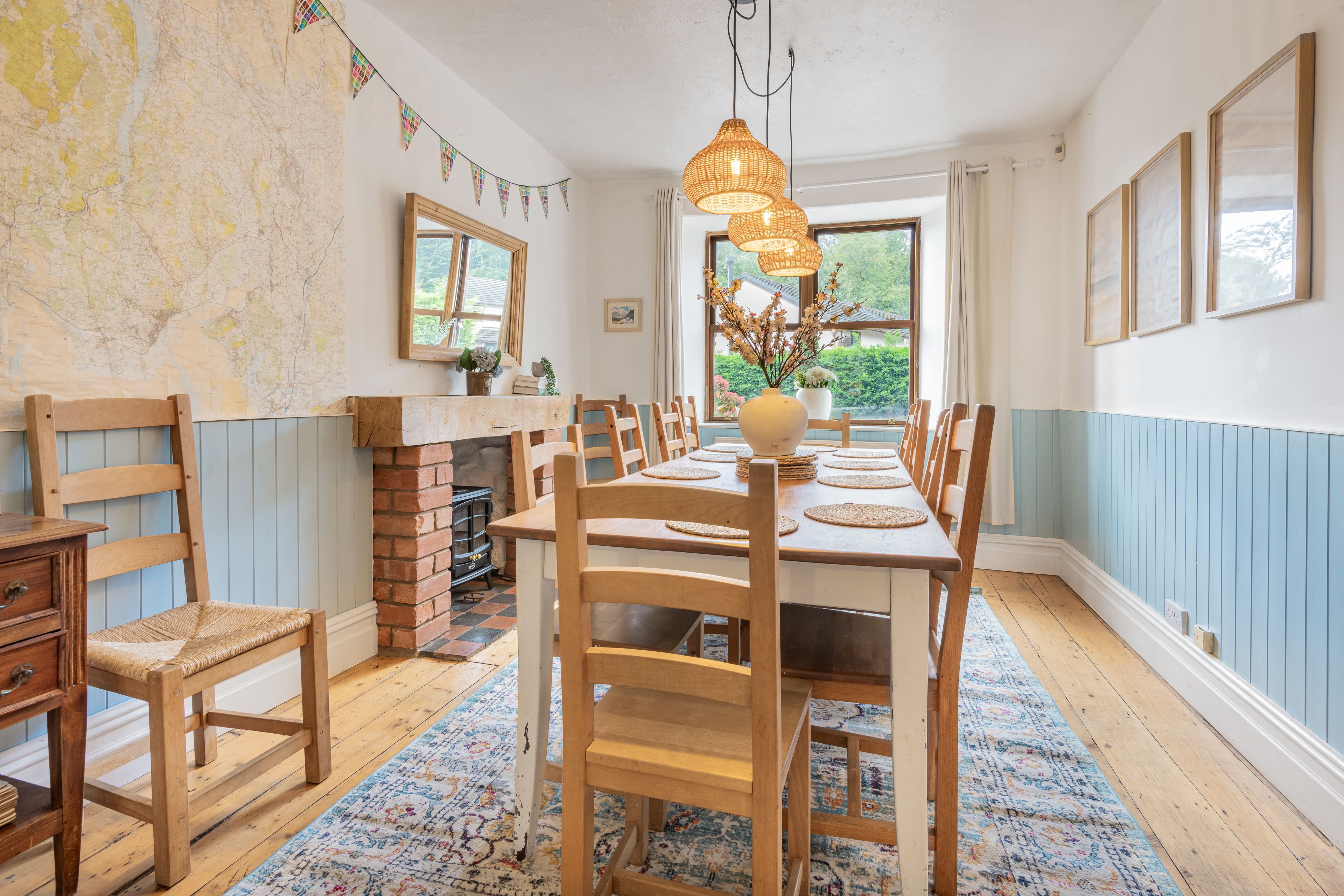 A dining room with a long wooden table, chairs, a brick fireplace, and a map on the wall.