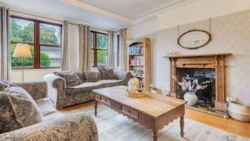 A cozy living room with a fireplace, a sofa set, a wooden coffee table, and a bookshelf.
