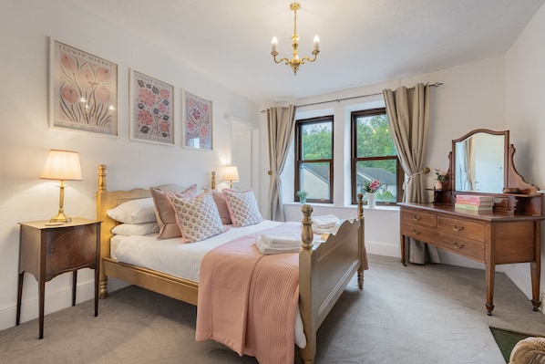 Un dormitorio con cama, mesitas de noche, cómoda, espejo y cuadros en la pared.