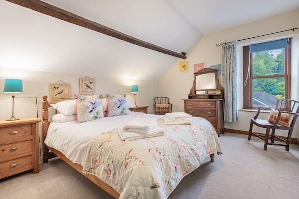 Een slaapkamer met een groot bed, twee nachtkastjes, een kaptafel, een stoel en een raam met gordijnen.