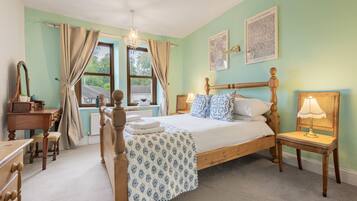 A bedroom with a wooden bed, a desk, a chair, a lamp, and two framed pictures on the wall.