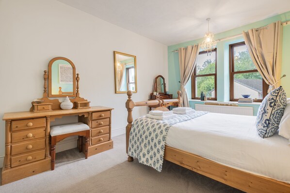A bedroom with a wooden bed, a bedside table, a dresser, two mirrors, and a window with curtains.