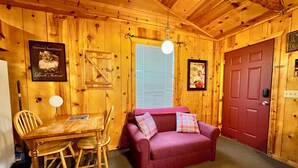 A cozy cabin interior with a wooden dining table, chairs, a red door, and a purple sofa with plaid cushions. - Liberty Cabin Number 301 (Mountain View)