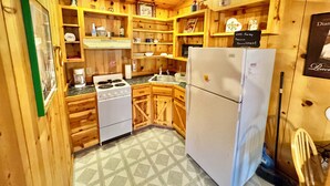 A wooden cabin-style kitchen with a stove, refrigerator, and various kitchen items on shelves. - Liberty Cabin Number 301 (Mountain View)