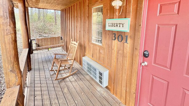 A wooden porch with a rocking chair and a bench, a red door, and a sign reading "LIBERTY 301". - Liberty Cabin Number 301 (Mountain View)