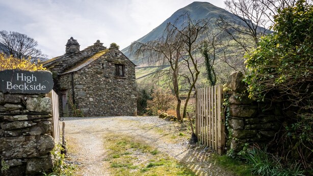 A stone cottage labeled "High Beckside" with a gravel path leading to it, surrounded by greenery and a mountain in the background.