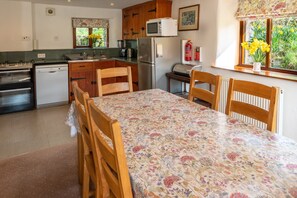 A kitchen with wooden cabinets, a stainless steel refrigerator, a microwave, and a dining table with floral tablecloth. - High Beckside -  Traditional Lakeland Cottage near Ullswater. Sleeps up to 7 guests (Penrith)