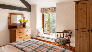 A bedroom with a wooden dresser, a chair, a window seat, and a bed.