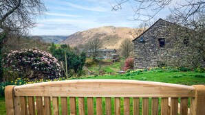 A wooden bench in a garden with a stone building and a valley in the background.