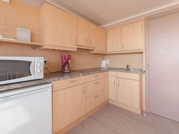 A kitchen with wooden cabinets, a microwave, a coffee maker, and a refrigerator.
