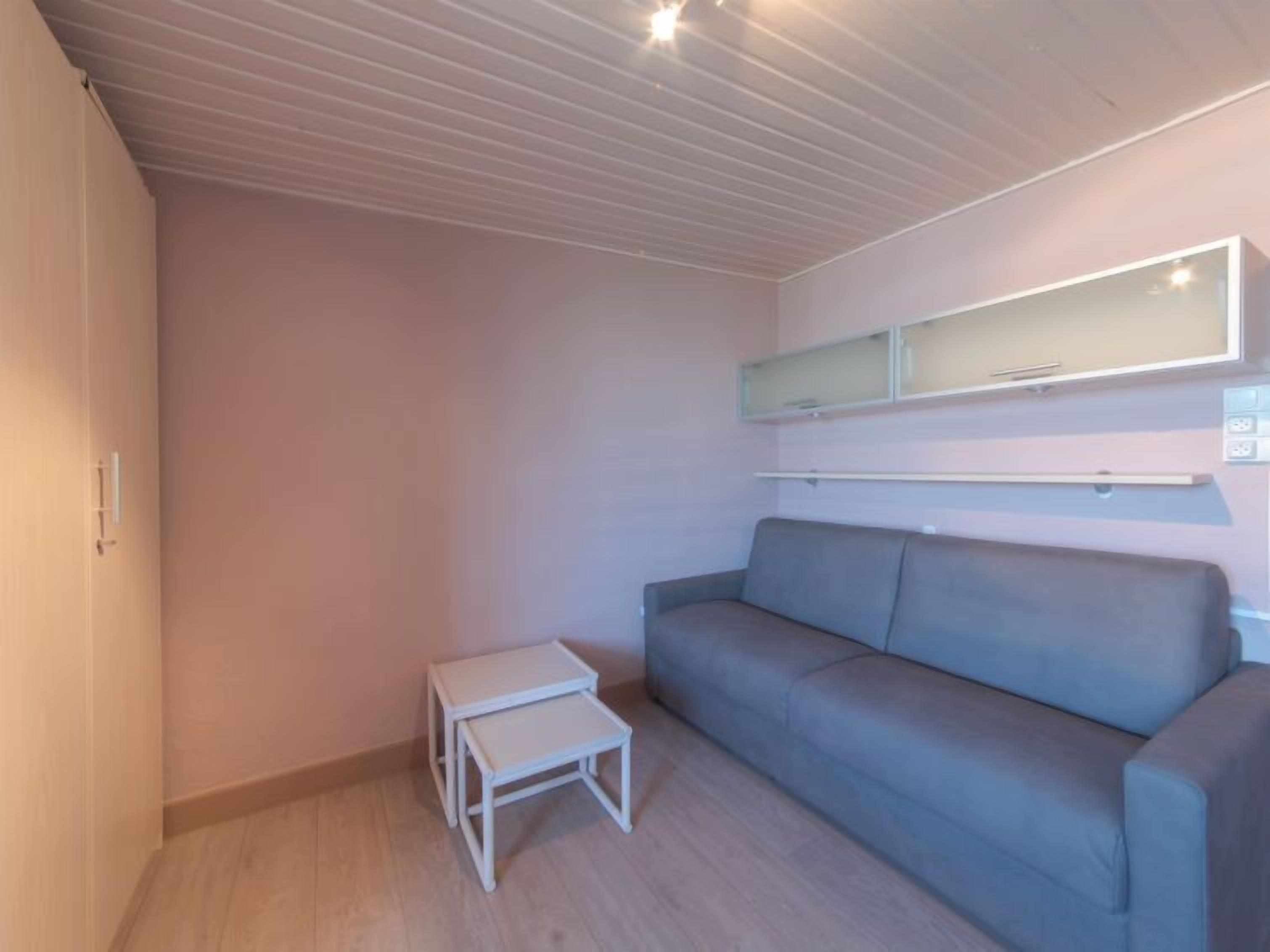 A modern, minimalist room with a grey sofa, a small white table, and a ceiling with linear lighting.