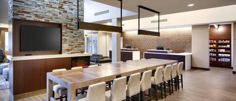 A modern kitchen with a long dining table, built-in appliances, and a brick accent wall.