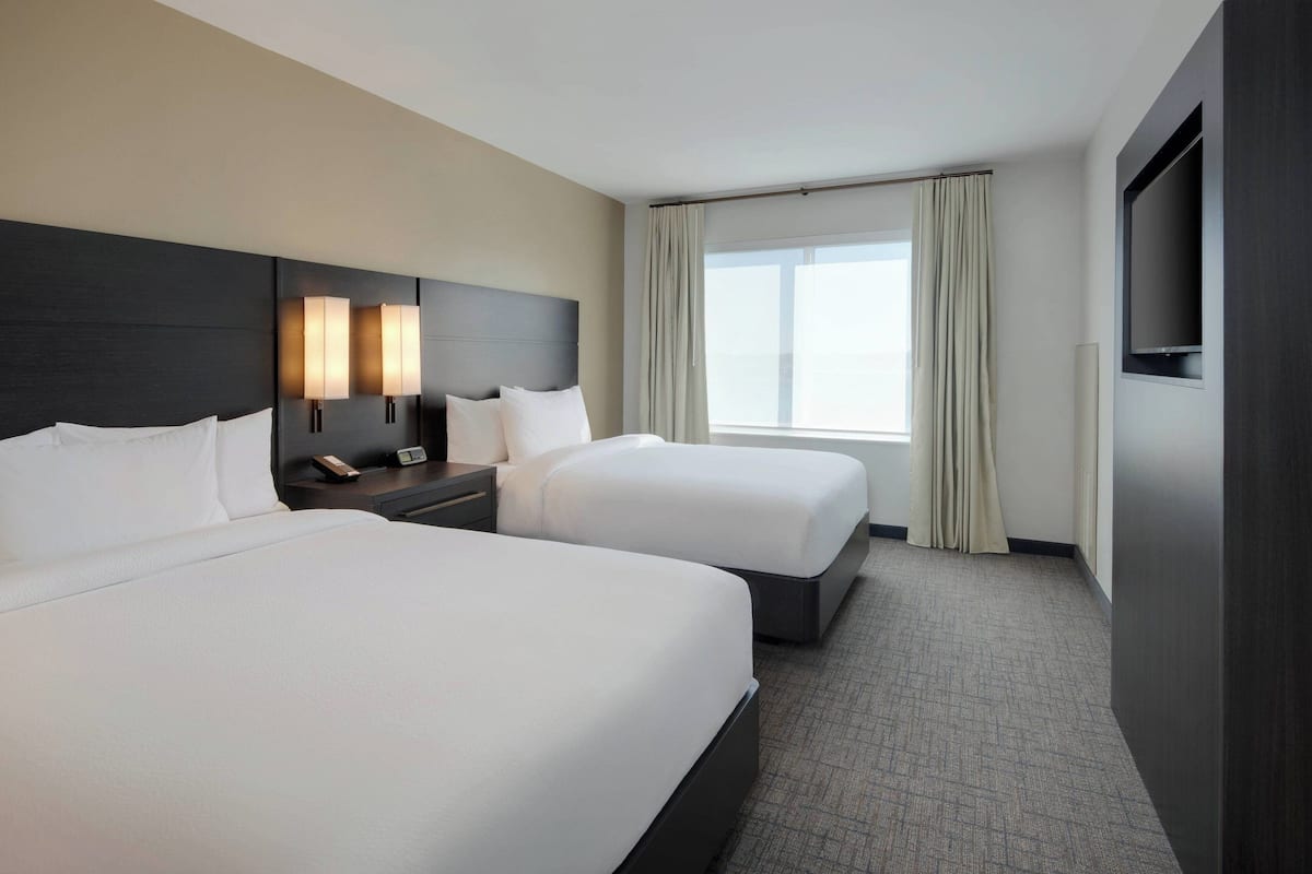 A hotel room with two beds, a TV, a nightstand, and a window with curtains.