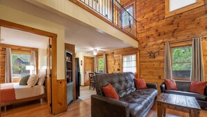 A wooden cabin interior with a loft bedroom, a living room with a sofa and coffee table, and a dining area. - ER24 - Honeysuckle Holler | Great Location..Close to town (Pigeon Forge)