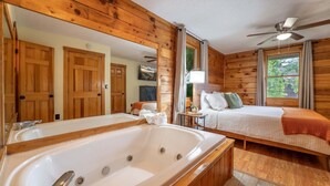 A wooden cabin interior with a large bathtub, a bed with a view, and a ceiling fan. - ER24 - Honeysuckle Holler | Great Location..Close to town (Pigeon Forge)