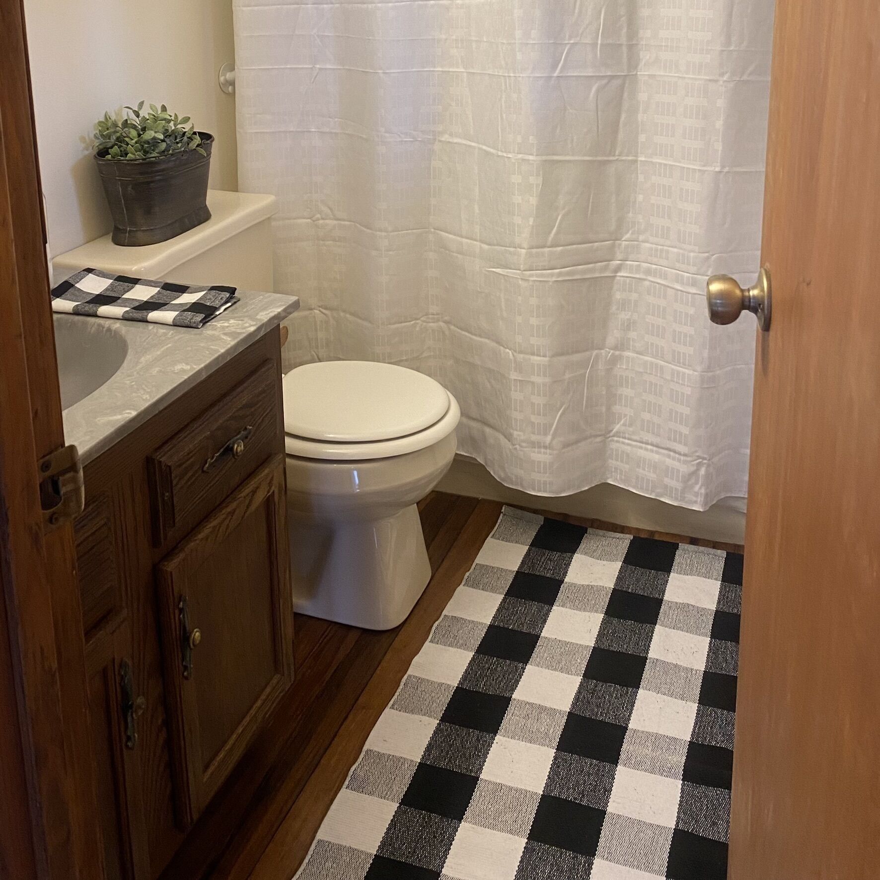 Une salle de bain avec des toilettes, un lavabo, un rideau de douche et un tapis de sol à carreaux.