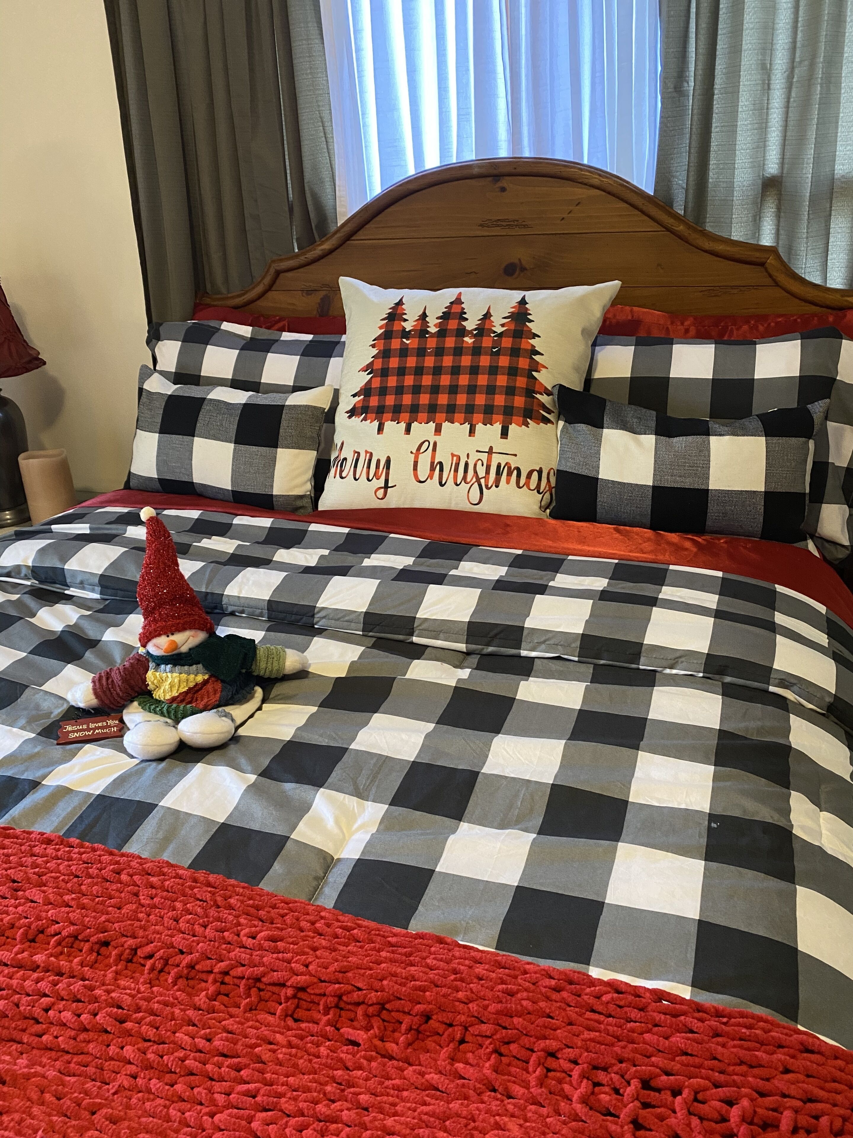 Un lit avec une couvre-lit à carreaux, un coussin orné du mot « Joyeux Noël » et une décoration représentant un bonhomme de neige.