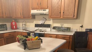 A kitchen with wooden cabinets, a white countertop, a red kettle, a gas stove, and a fruit basket. - Blue Ridge Mountain Air (Old Fort)