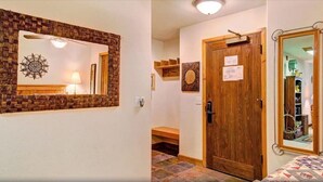 A hallway with a woven wall hanging, a wooden door with a sign, and a mirror reflecting a room with a bed.