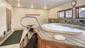 A hot tub with a wooden deck, a clock, and a stone wall.
