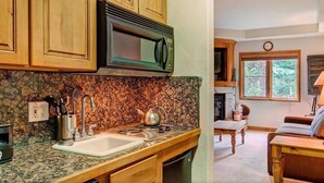 A kitchen with granite countertops, wooden cabinets, a microwave, and a sink.