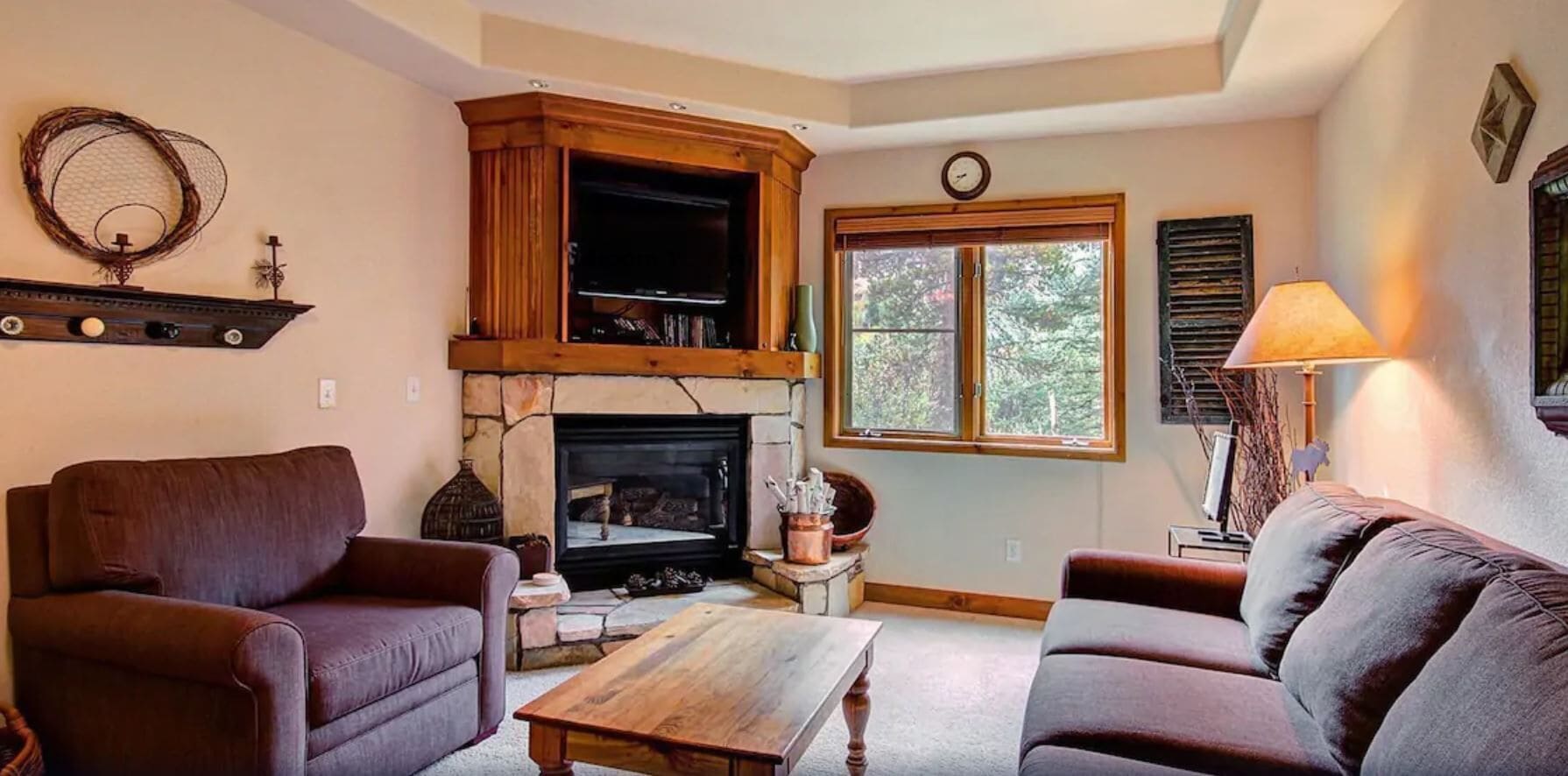A cozy living room with a fireplace, two sofas, a coffee table, and a TV.
