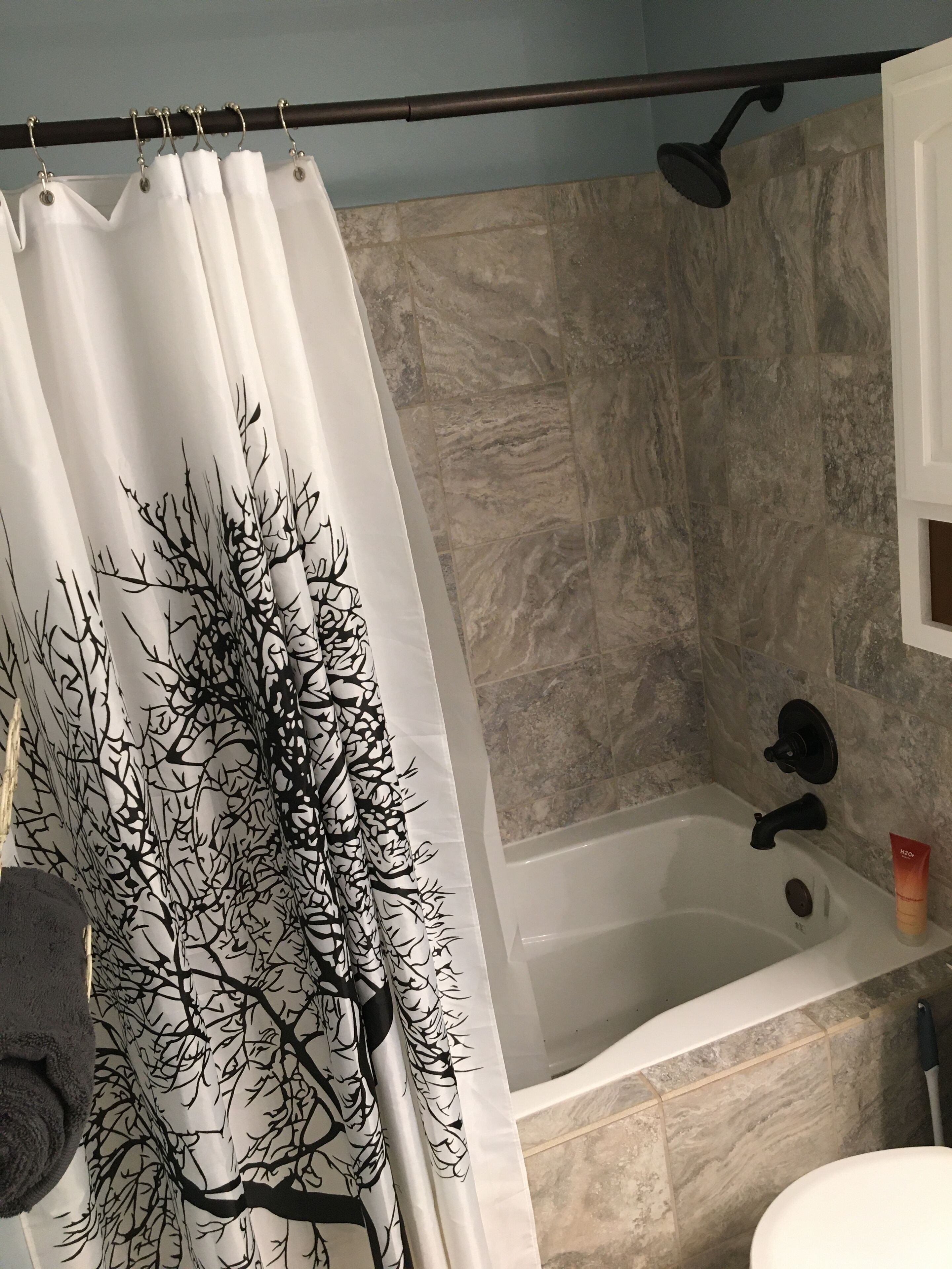 A bathroom with a shower curtain featuring a black tree pattern, a bathtub, and a towel rack.