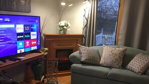 Ein Wohnzimmer mit Sofa, Fernseher, der Streaming-Dienste zeigt, Kamin und einem fenster mit Vorhängen.