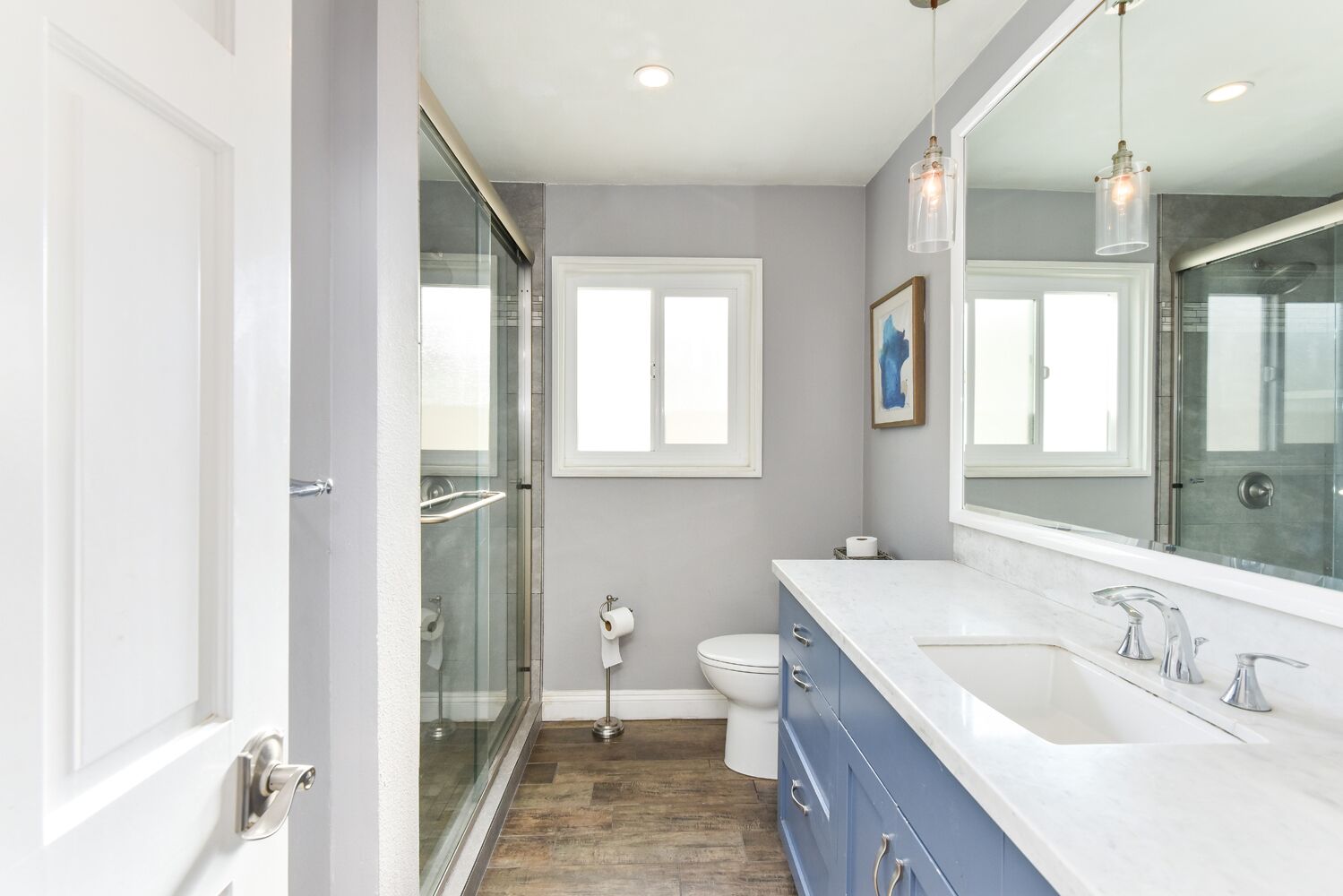 A modern bathroom with a glass shower enclosure, a white toilet, and a large mirror above the sink.