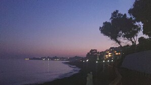 Uma passarela costeira ao entardecer, com guarda-corpo e luzes urbanas ao longe.