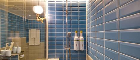 Un baño con paredes de azulejos azules, una cabina de ducha de cristal y artículos de aseo en el lavamanos.