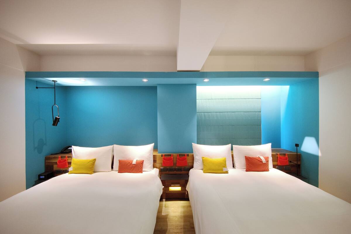 A hotel room with two beds, a wooden headboard, and a blue accent wall.