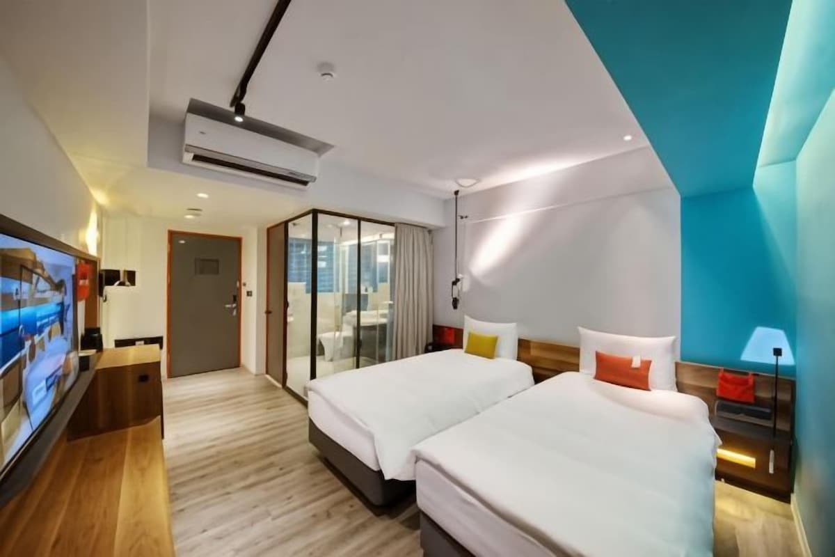A modern hotel room with two beds, a TV, a desk, and a sliding glass door leading to a balcony.