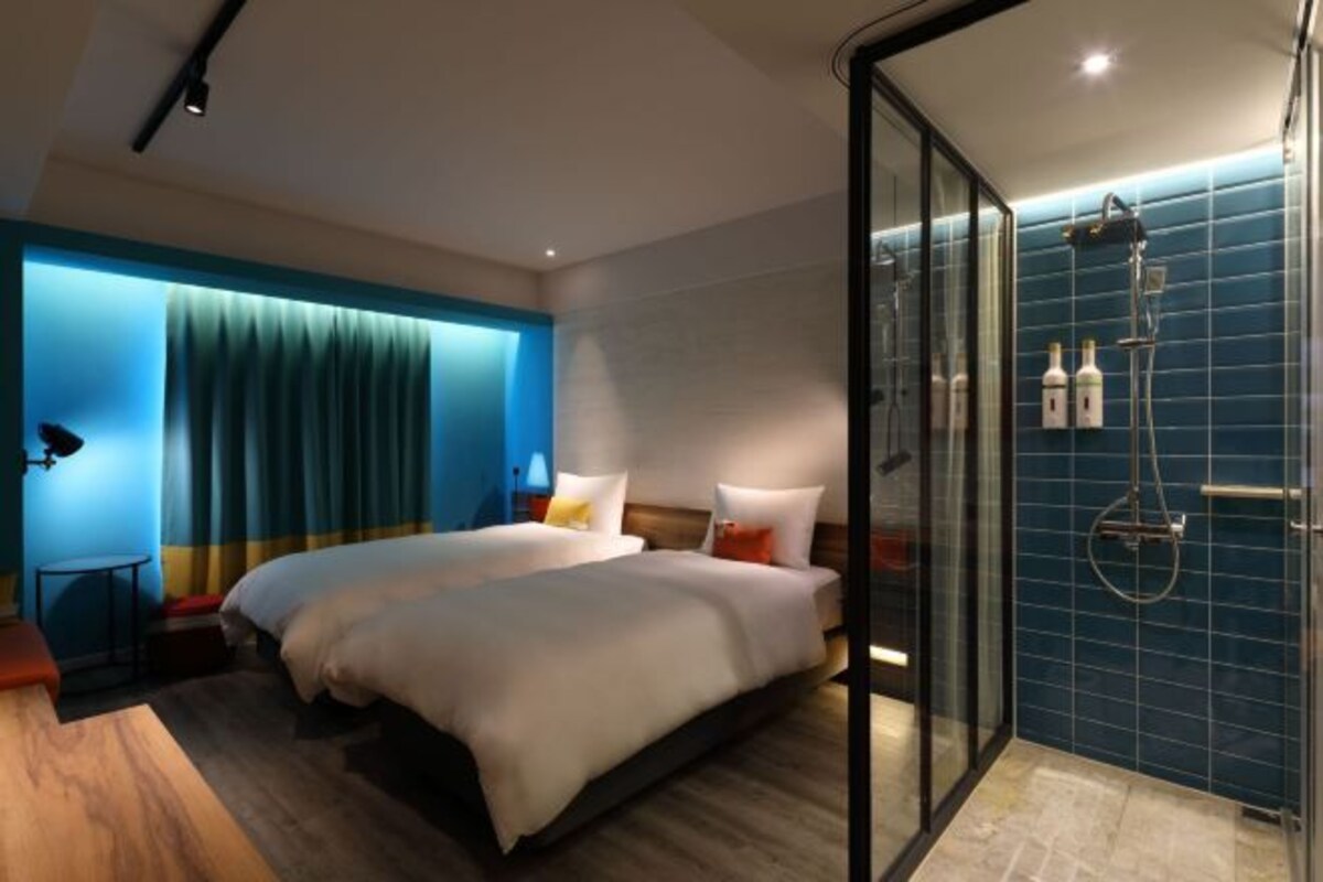 A hotel room with two beds, a glass shower enclosure, and a blue-tiled shower area.