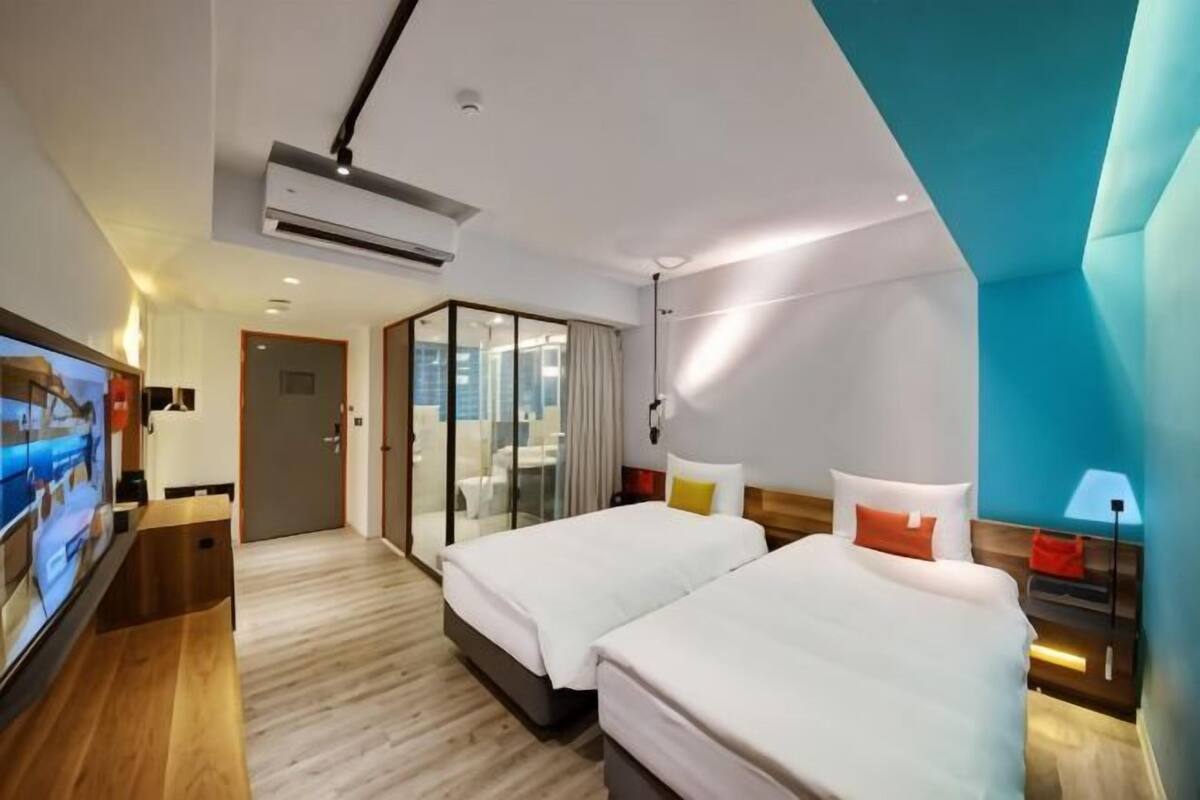 A modern hotel room with two beds, a TV, a desk, and a sliding glass door leading to a balcony.