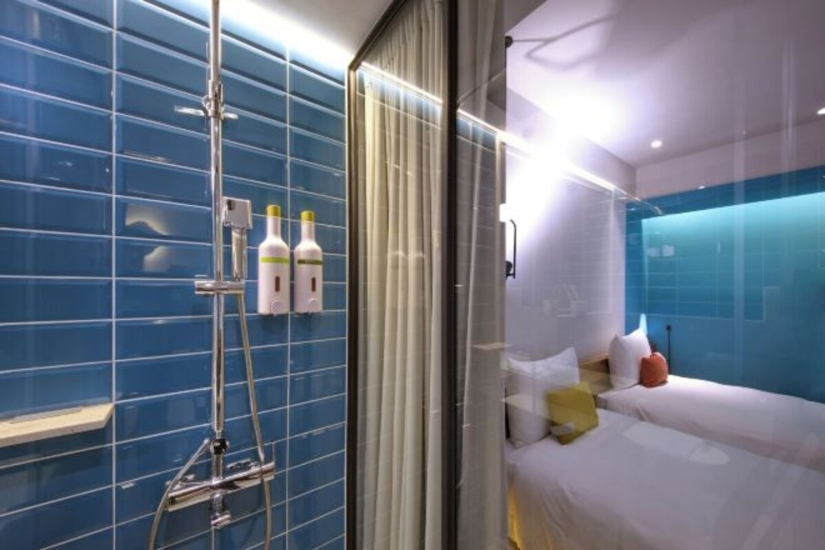 A modern hotel room with a large bed, a shower area with a glass door, and a blue-tiled wall.