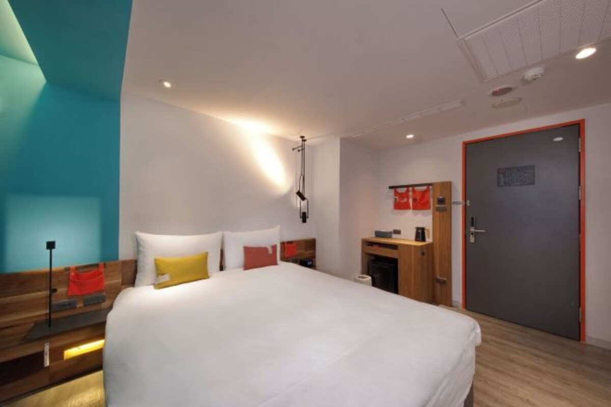 A modern hotel room with a large bed, bedside tables, a desk, and a wardrobe.
