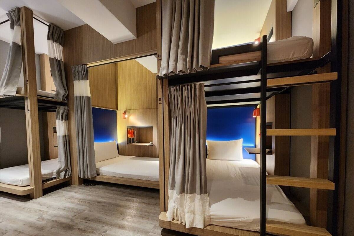 A hotel room with bunk beds, wooden flooring, and a nightstand with a lamp.