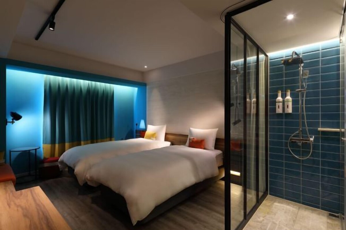 A hotel room with two beds, a glass shower enclosure, and a blue-tiled shower area.