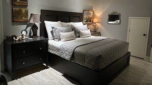 Un dormitorio con cama, mesitas de noche, cómoda y ventilador de techo, además de obras de arte en las paredes.