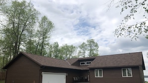 A two-story wooden house with a garage, a covered porch, and a small outdoor seating area.