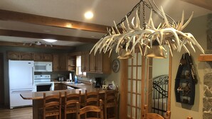 A kitchen with wooden cabinets, a white refrigerator, a wooden dining table with chairs, and a chandelier made of antlers.