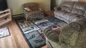 A living room with a floral armchair, a large sofa, and a patterned rug.