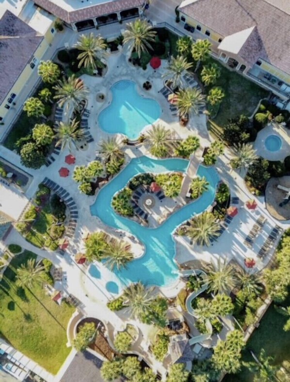 An aerial view of a resort with multiple swimming pools, palm trees, and lounge areas.