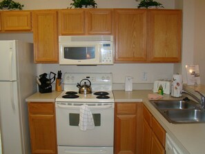 A kitchen with wooden cabinets, a white stove, a microwave, a kettle, and a sink.