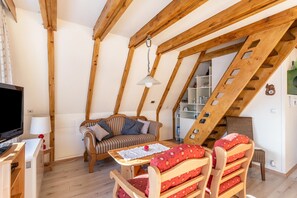 A cozy room with a wooden ceiling, a sofa, a table with a red cushion, a TV, and a lamp.