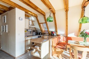 A kitchen with wooden beams, a clock, and a dining area with a bench and table.