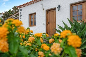 A white building with a wooden door and windows, surrounded by yellow flowers.