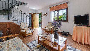 Un salon avec un escalier, un téléviseur, un canapé, une table basse et un fauteuil.