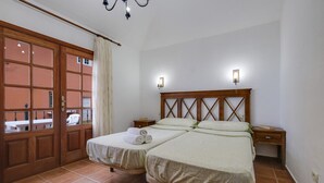 Ein Doppelbett mit Holz Kopfteil, zwei Nachttische, ein Fenster mit Vorhängen und Blick auf ein Gebäude.